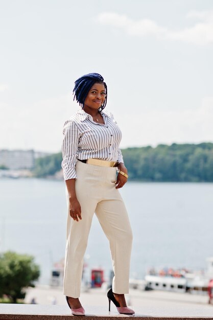Elegante donna d'affari afroamericana in pantaloni e camicetta poste all'aperto contro il lago