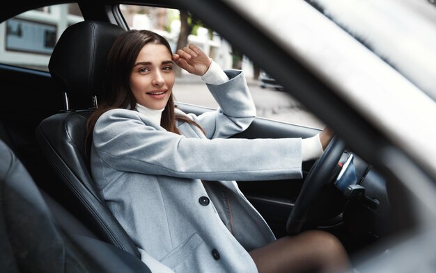 Elegante donna d'affari che guida un'auto sorridendo felice Dirigente femminile attraente che si dirige a lavorare nel suo veicolo