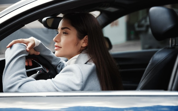 Elegante donna d'affari seduto nella sua macchina e in attesa di qualcuno che guarda la strada della città Autista donna che guarda pensieroso fuori dalla finestra