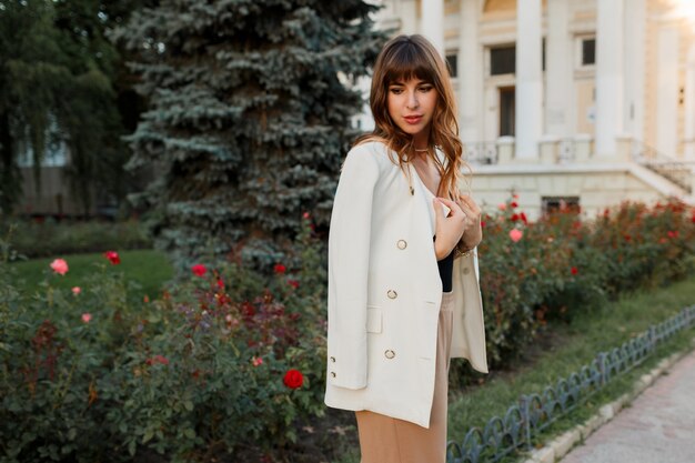 Elegante donna europea con i capelli ondulati in posa sulla strada. Look elegante.