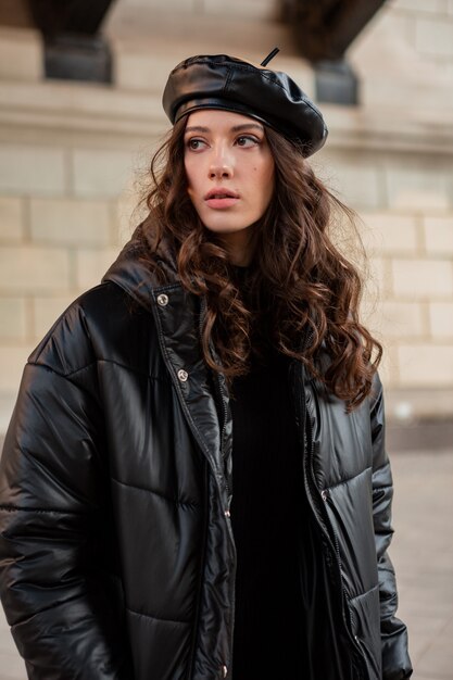 Elegante donna in posa in inverno autunno moda tendenza nero piumino e berretto in pelle cappello in vecchia bella strada