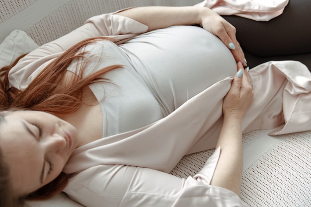 Elegante donna incinta nell'ultimo mese che riposa sul divano di casa si chiuda.
