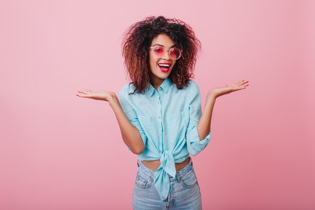 Elegante donna nera in abbigliamento casual che esprime emozioni sorprese. Splendida ragazza mulatta dai capelli corti in posa in camicia blu.