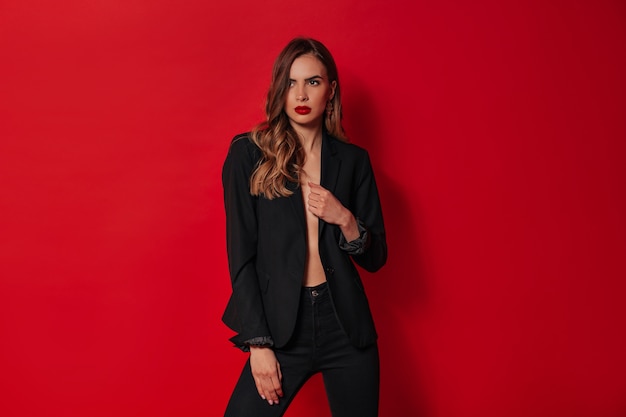 Elegante donna sicura di sé in abito nero in posa sopra la parete rossa
