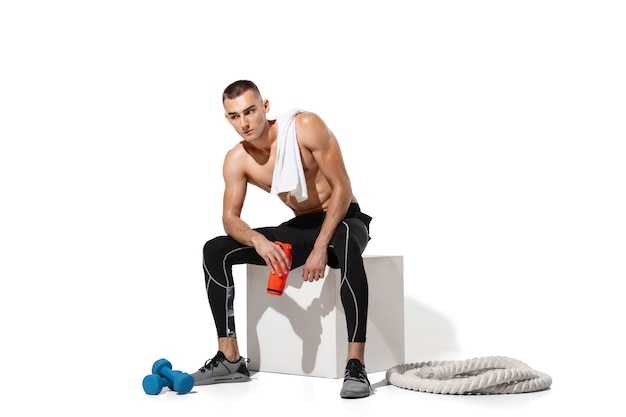 Elegante giovane atleta maschio praticando su sfondo bianco studio, ritratto con le ombre. Modello dalla vestibilità sportiva che si allena in movimento e in azione.