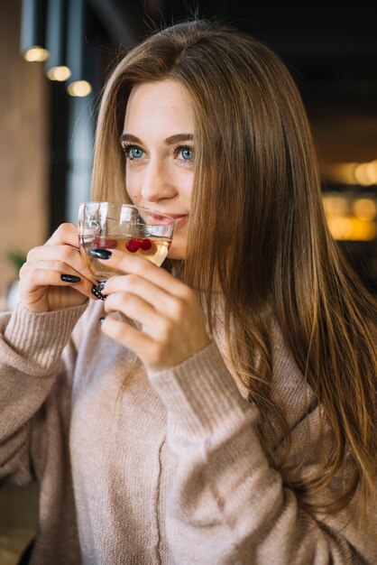 Elegante giovane donna sorridente che beve dalla tazza nella caffetteria