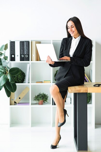 Elegante giovane imprenditrice seduto sulla scrivania utilizzando il computer portatile