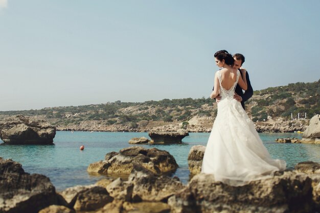 Elegante giovane sorridente sposa e sposo posa sulle rocce sulla spiaggia