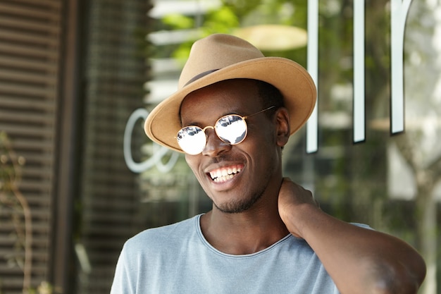 Elegante giovane uomo che indossa cappello e occhiali da sole