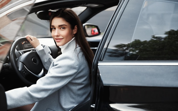 Elegante imprenditrice entra in macchina per guidare il lavoro Donna d'affari sorridente apre la portiera del veicolo e guarda la fotocamera