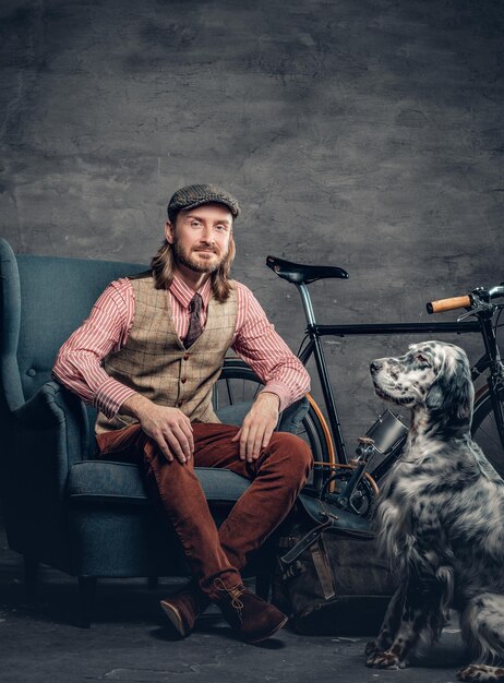 Elegante maschio con capelli lunghi in posa con setter irlandese e bicicletta a velocità singola.