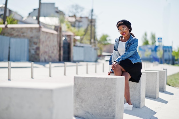 Elegante modello afroamericano in giacca di jeans cappello occhiali e gonna nera poste all'aperto