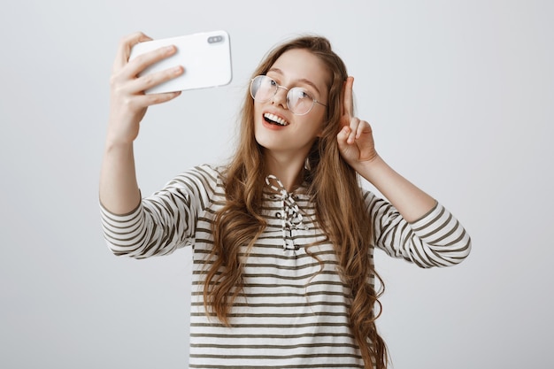 Elegante ragazza adolescente prendendo selfie sullo smartphone, sorridendo felice