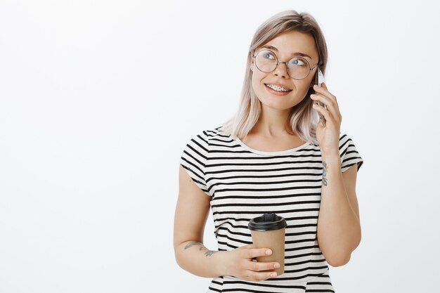 Elegante ragazza bionda rilassata in posa in studio con il suo telefono e caffè