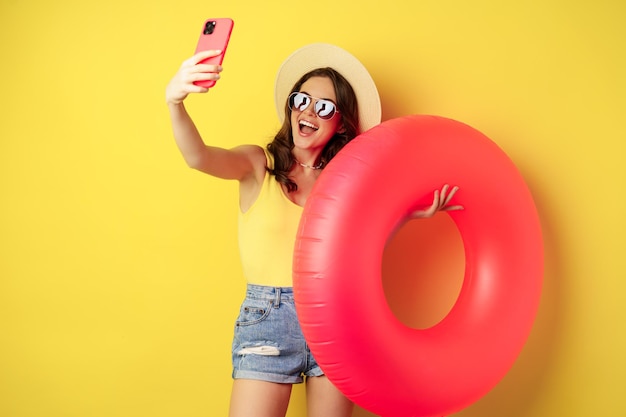 Elegante ragazza bruna in vacanza che si fa selfie con l'anello di nuotata che va sulla spiaggia nuotando in mare sulla somma...