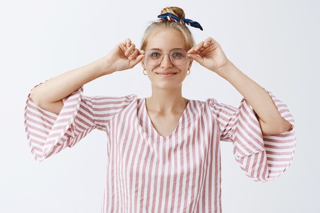 Elegante ragazza moderna con gli occhiali in posa contro il muro bianco