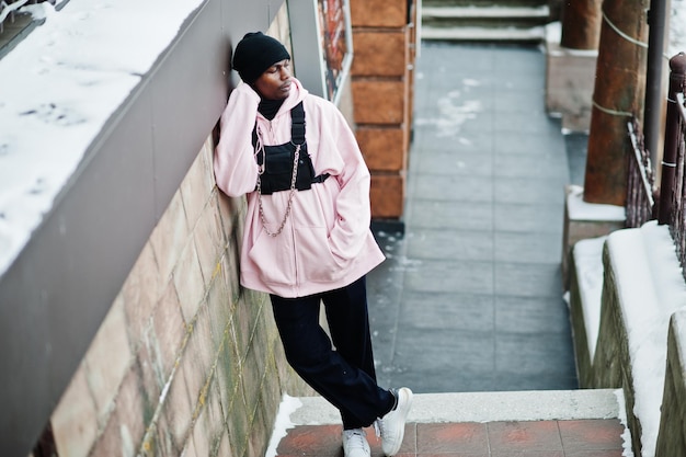 Elegante uomo afroamericano in stile urbano con felpa con cappuccio rosa in posa al giorno d'inverno