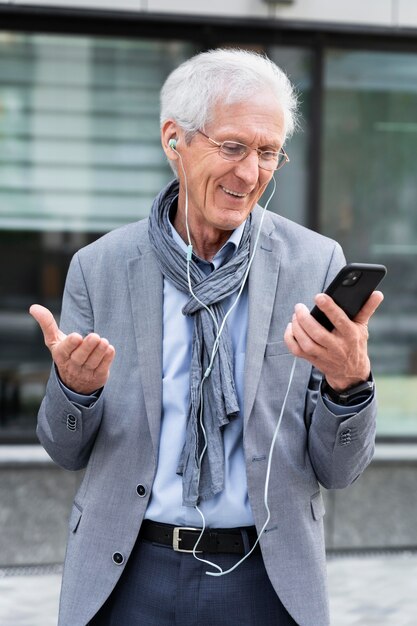 Elegante uomo anziano in città che utilizza smartphone e auricolari per la videochiamata