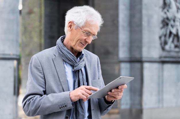 Elegante uomo anziano in città che utilizza tablet