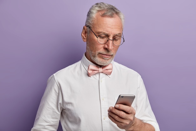 Elegante uomo anziano lavora sul suo telefono, concentrato nel display cerca di capire come utilizzare le moderne tecnologie