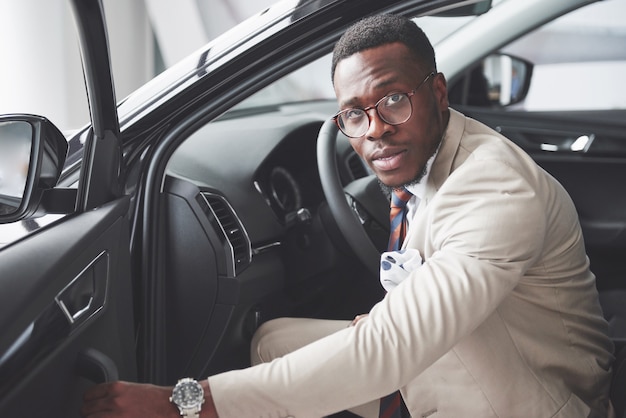 Elegante uomo d'affari nero seduto al volante della nuova auto di lusso. Ricco uomo afroamericano.