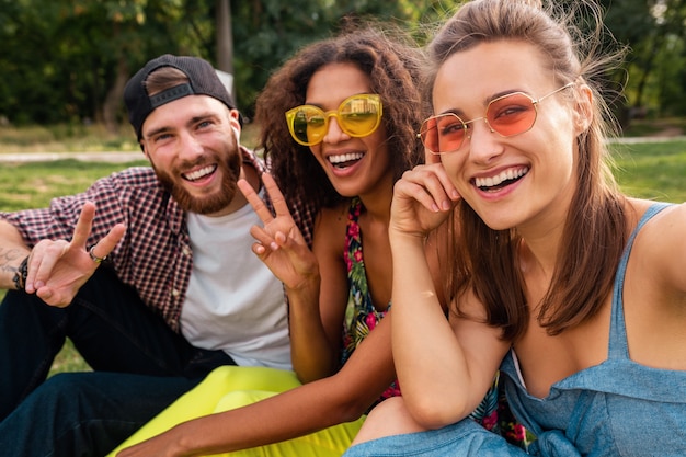 Eleganti giovani amici felici seduti al parco, facendo selfie