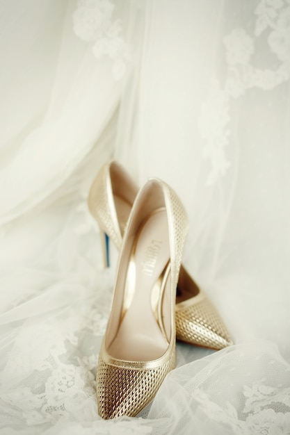 Eleganti scarpe dorate stanno sul velo da sposa in pizzo