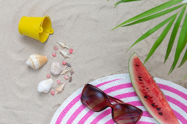 Elementi spiaggia sulla sabbia con anguria e occhiali da sole