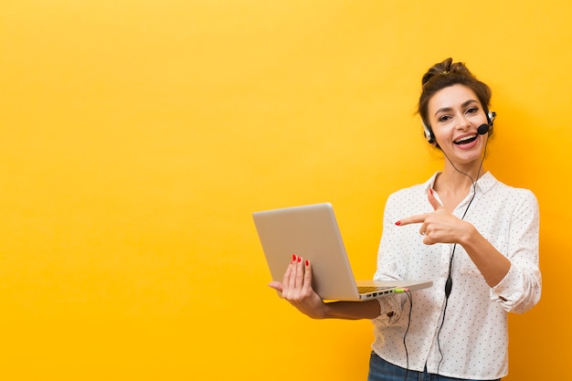 Emoticon donna che indossa l'auricolare e che punta al computer portatile che sta tenendo