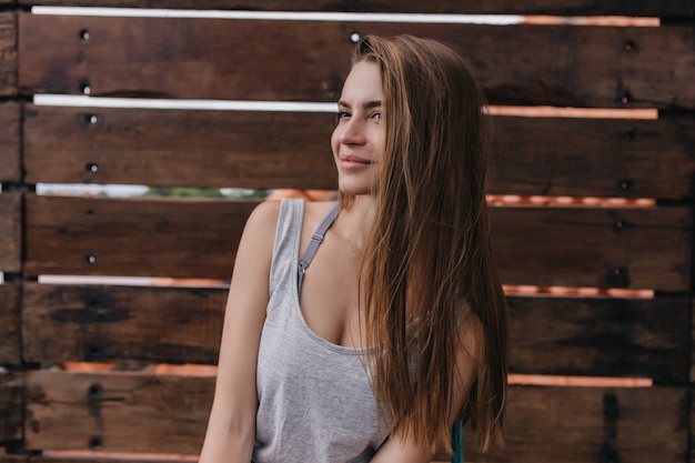 Emotiva donna bianca con i capelli lunghi in posa nella calda mattina di primavera. Foto della meravigliosa ragazza caucasica isolata sulla parete di legno.