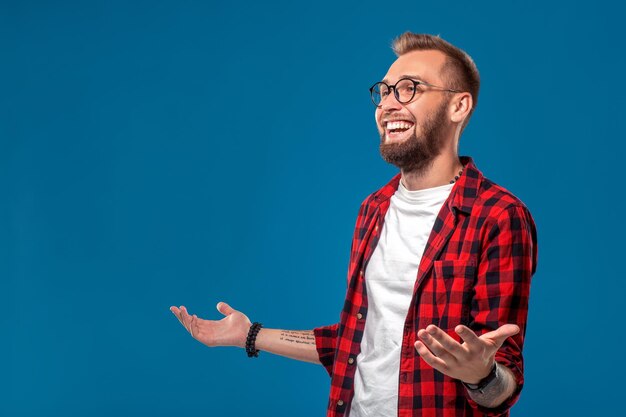 Emotivo e concetto di persone: giovane uomo barbuto in camicia a scacchi. Stile hipster. Studio girato su sfondo blu. Copia spazio