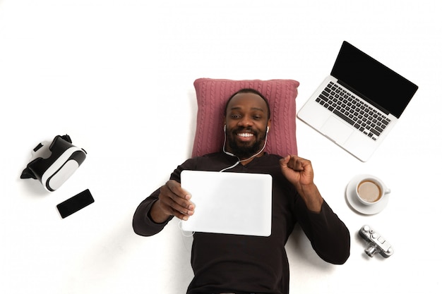 Emotivo uomo afro-americano con gadget, tecnologie. Dispositivi che collegano le persone durante la quarantena