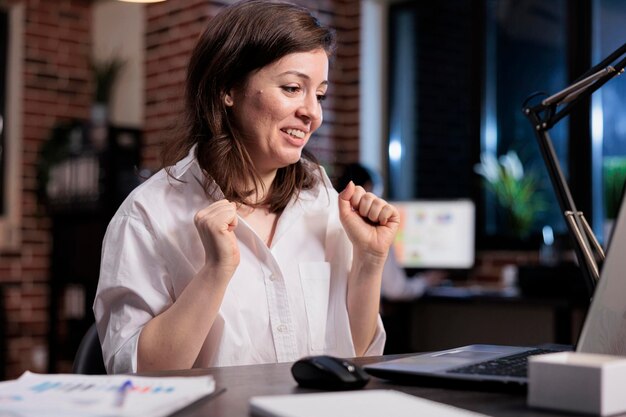 Emozionante consulente finanziario gioioso che celebra un affare di successo mentre è seduto alla scrivania nell'area di lavoro dell'ufficio. Donna di affari eccitata felice che sorride con gioia a causa della campagna di promozione positiva.