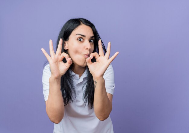 Emozionato giovane ragazza bruna caucasica gesti il segno giusto della mano con due mani isolate sulla parete viola