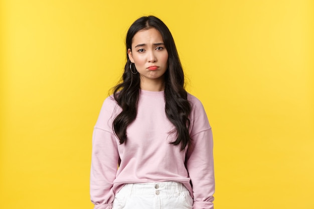 Emozioni della gente, stile di vita e concetto di moda. Depressa e triste, cupa ragazza coreana che fa il broncio, guardando giù nelle discariche, sentendosi sconvolta e scontenta, in piedi sfondo giallo.