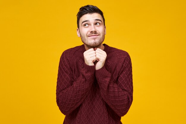 Emozioni umane positive, sentimenti ed espressione facciale. Foto di un bel giovane uomo europeo con i capelli scuri e la barba incolta che osserva in su con il sorriso misterioso sveglio, tenendosi per mano al suo fronte, sognando