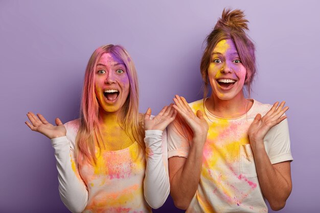 Emtional felici migliori amiche usano la tintura colorata durante il festival di Holi, spalmate di polvere arcobaleno colorato, allargano le palme dalla felicità e dal divertimento, celebrano le vacanze di primavera indiana, si inzuppano a vicenda