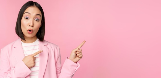 Entusiasta donna d'affari professionale commessa che punta il dito verso destra mostrando pubblicità o logo aziendale da parte in posa su sfondo rosa