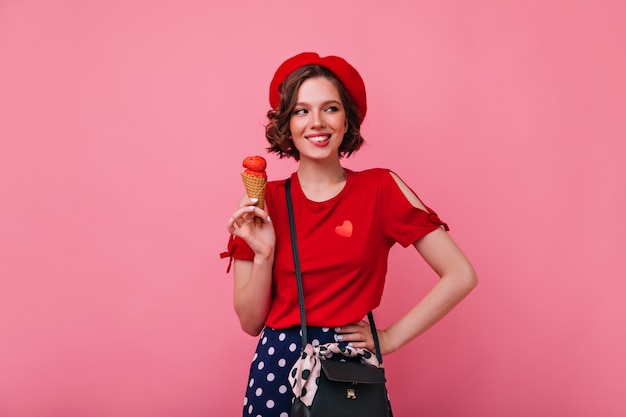 Entusiasta giovane donna in abiti alla moda che mangia il gelato. Foto interna di sorridente signora spensierata con dessert.