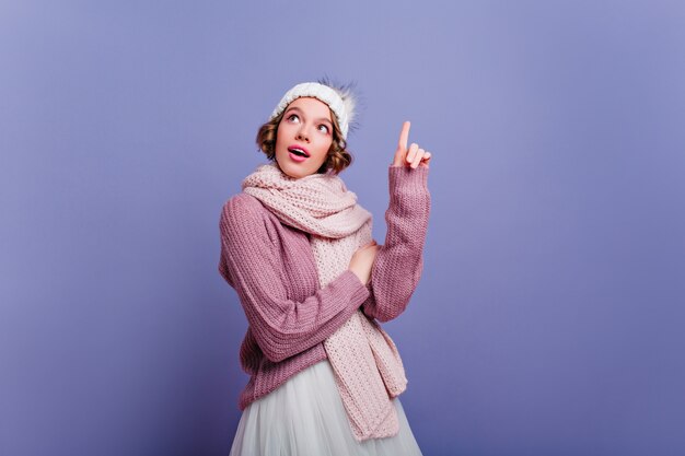 Entusiasta giovane signora con i capelli corti in posa in sciarpa lunga. Foto dell'interno di affascinante donna europea in abito invernale isolato sulla parete viola.