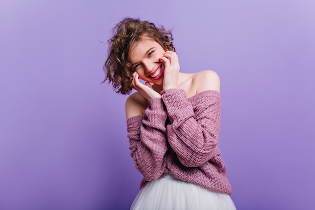 entusiasta ragazza bianca giocosamente in posa in abito. Ritratto dell'interno della donna dai capelli corti ispirata isolata sulla parete viola.