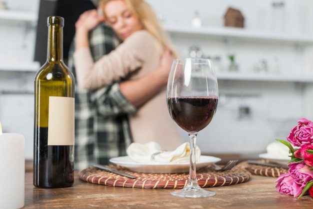 Equipaggi abbracciare con la donna vicino alla tavola con la bottiglia ed il bicchiere di vino