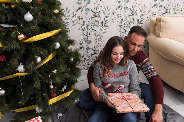 Equipaggi abbracciare la donna dalla parte posteriore con il regalo vicino all&#39;albero di Natale