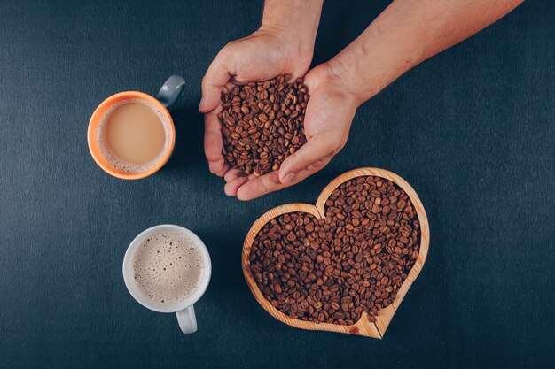 Equipaggi il caffè della tenuta con i chicchi di caffè in una ciotola a forma di cuore sul nero