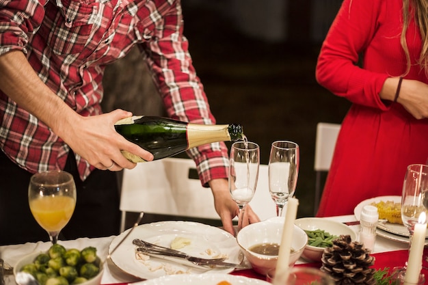 Equipaggi il champagne di versamento in vetro alla tavola festiva