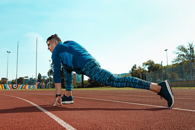 Equipaggi il corridore che allunga le gambe che preparano per l'addestramento di funzionamento sulle piste dello stadio che fanno il riscaldamento