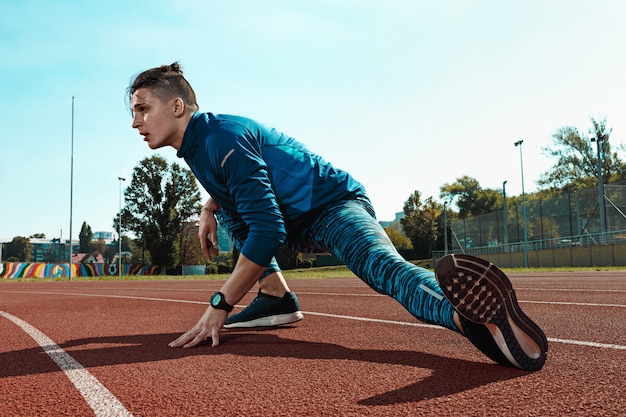 Equipaggi il corridore che allunga le gambe che preparano per l'addestramento di funzionamento sulle piste dello stadio che fanno il riscaldamento