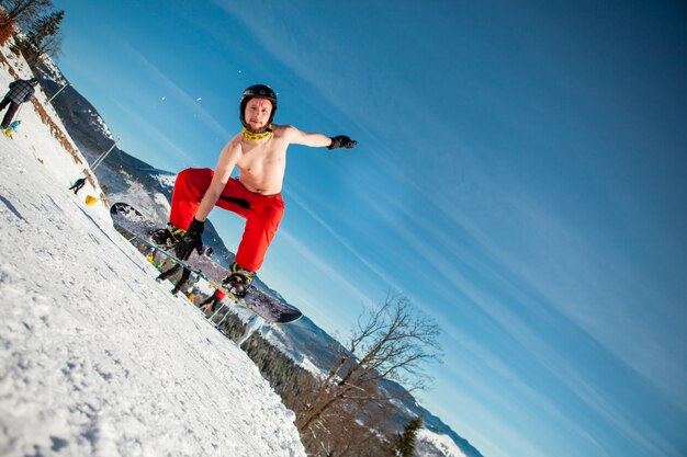 Equipaggi il pensionante che salta sul suo snowboard sullo sfondo delle montagne