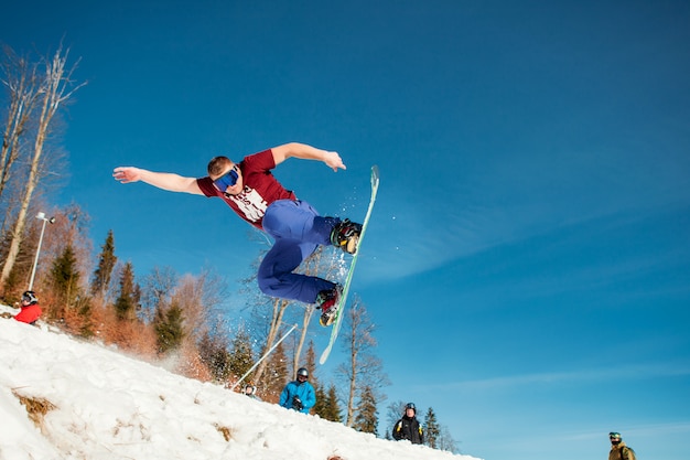 Equipaggi il pensionante che salta sul suo snowboard sullo sfondo delle montagne