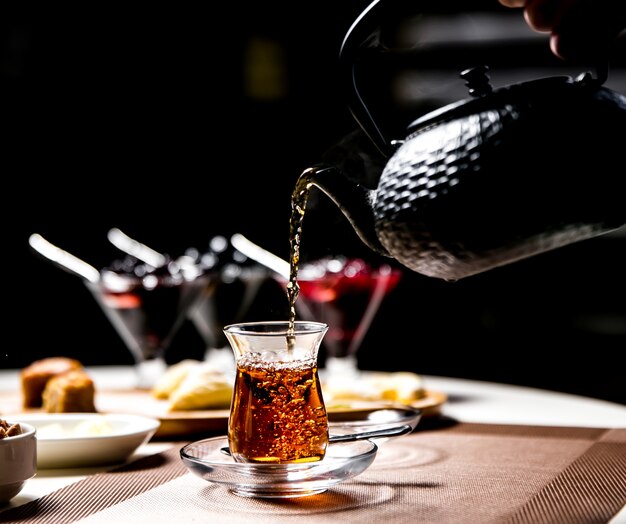 Equipaggi il tè nero di versamento nella vista laterale di vetro nazionale armudy